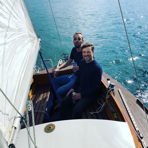 two guys in a wooden sailing boat drinking beer